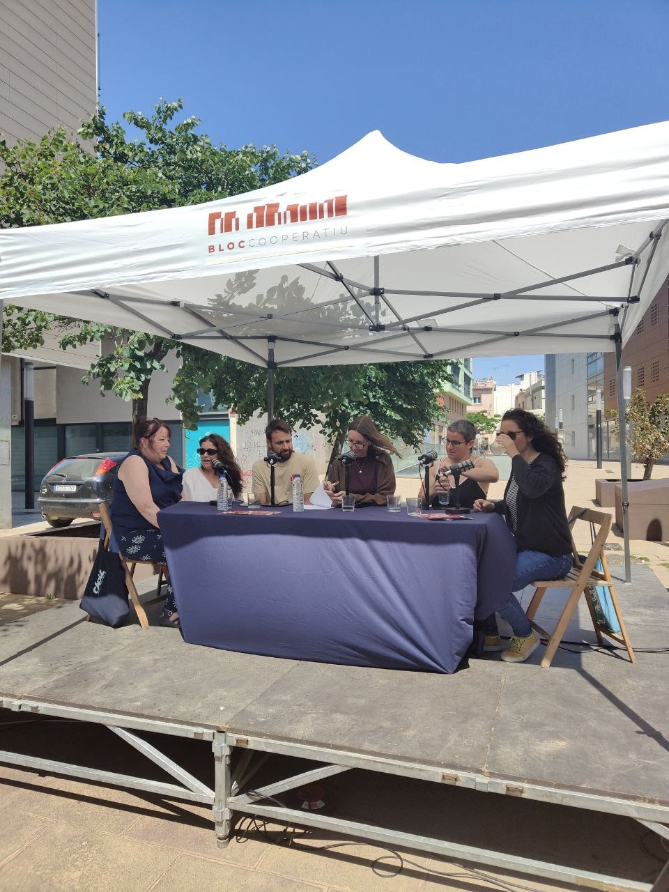 Members of La Llevantina at a round table with microphones, under a Bloc Cooperatiu marquee